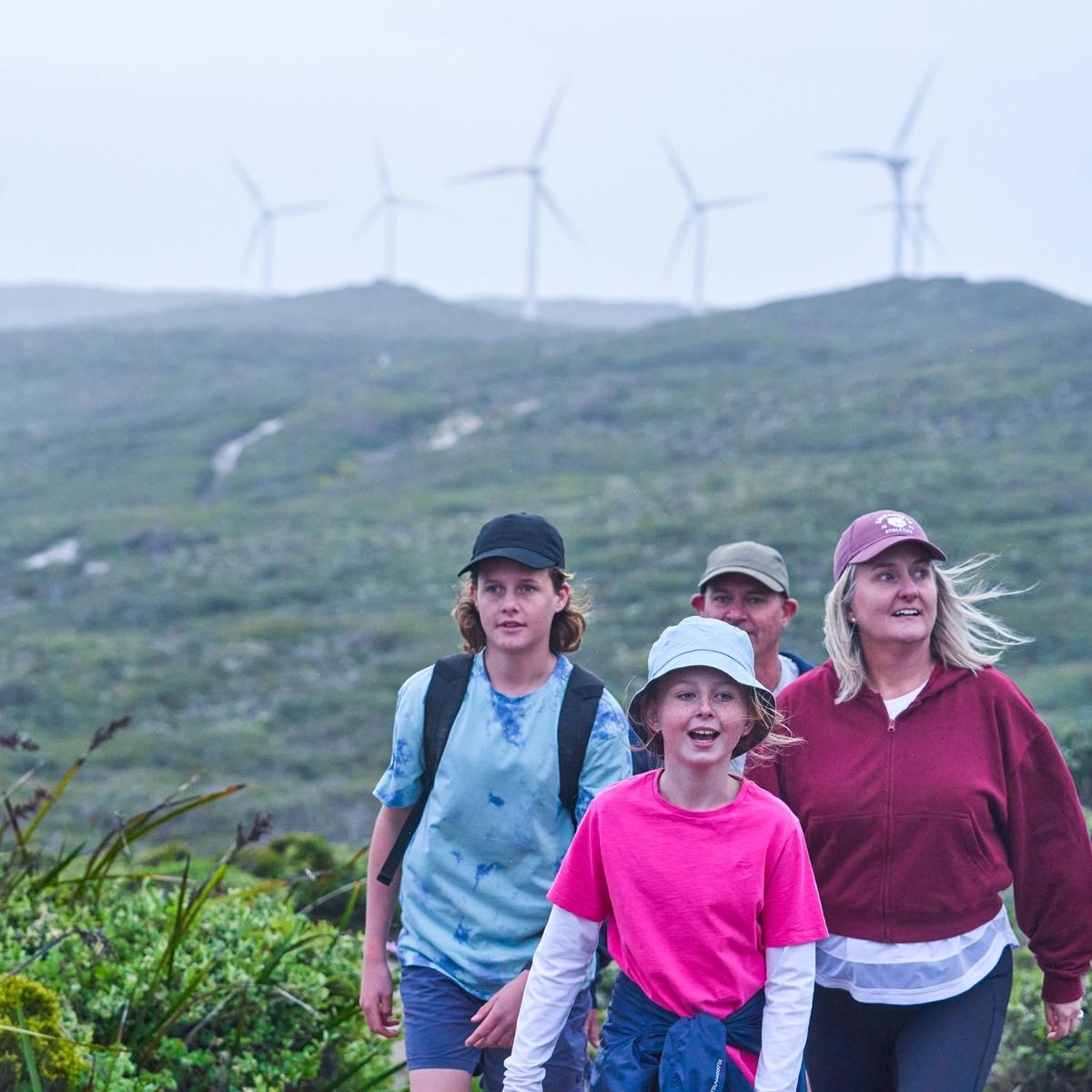 A family takes a walk at Albany wind farm with wind turbines in the distance